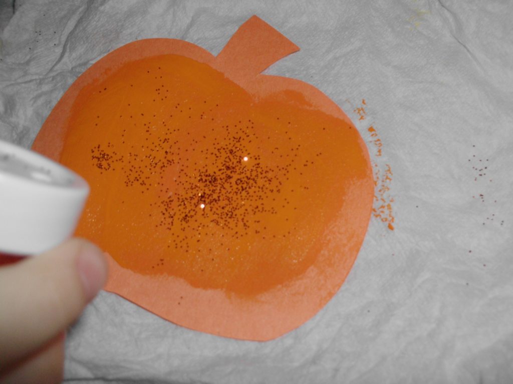 The paper pumpkin is getting glitter added to it