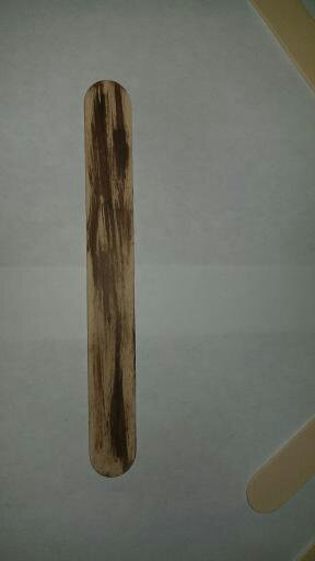 A popsicle stick that has been painted with brown paint to look like a piece of wood.