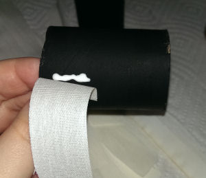 Toilet paper roll is painted black and is having bandage glued onto it.